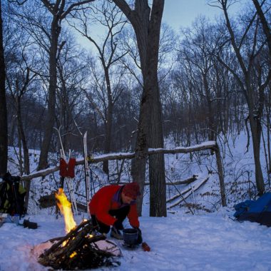 a man crouches over a pot in the snow