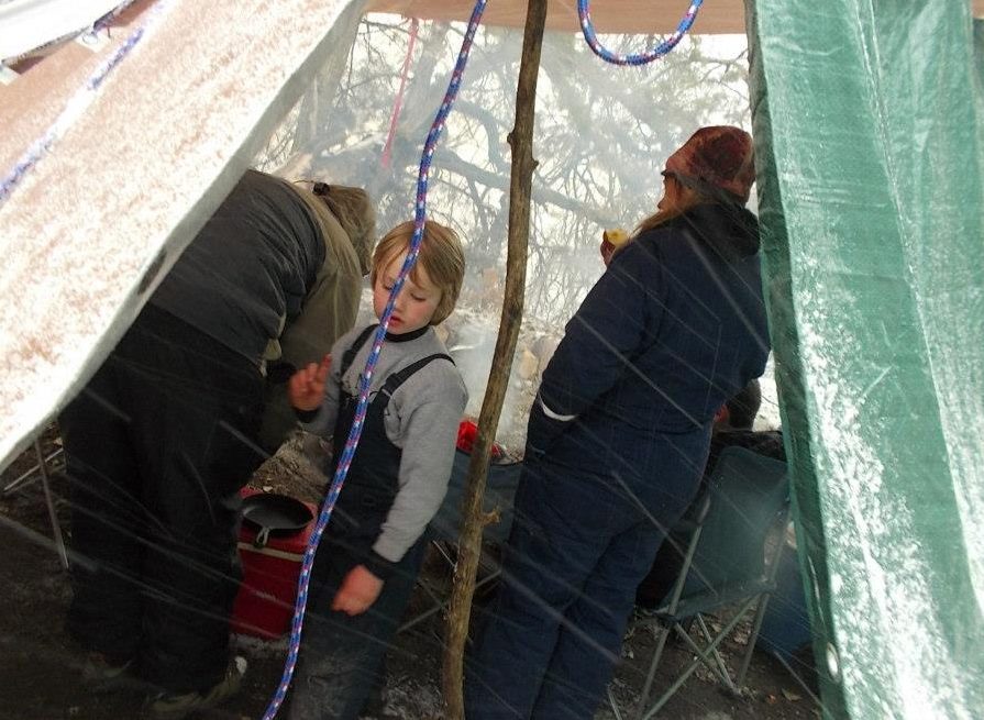 a boy walks through a tarped area of a campsite